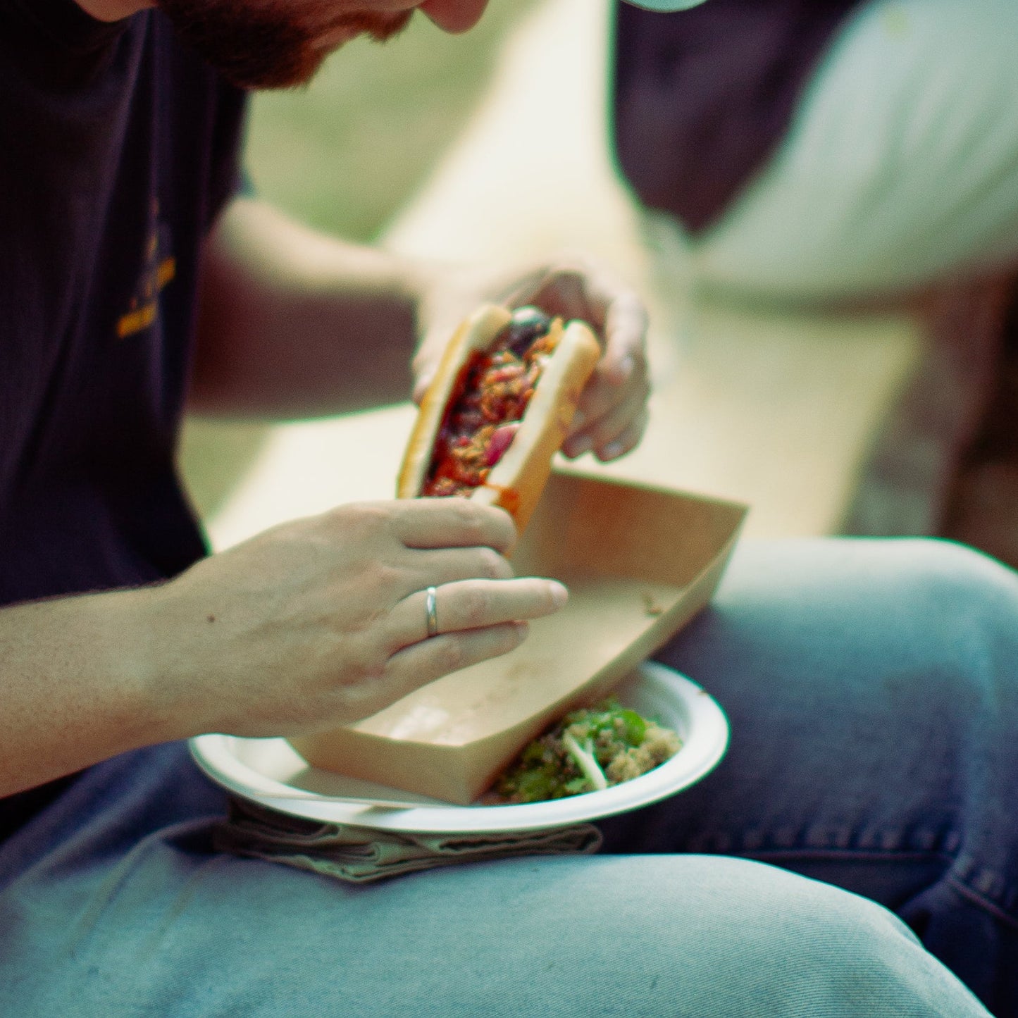 Two men sitting outdoors, eating food on a grassy area.